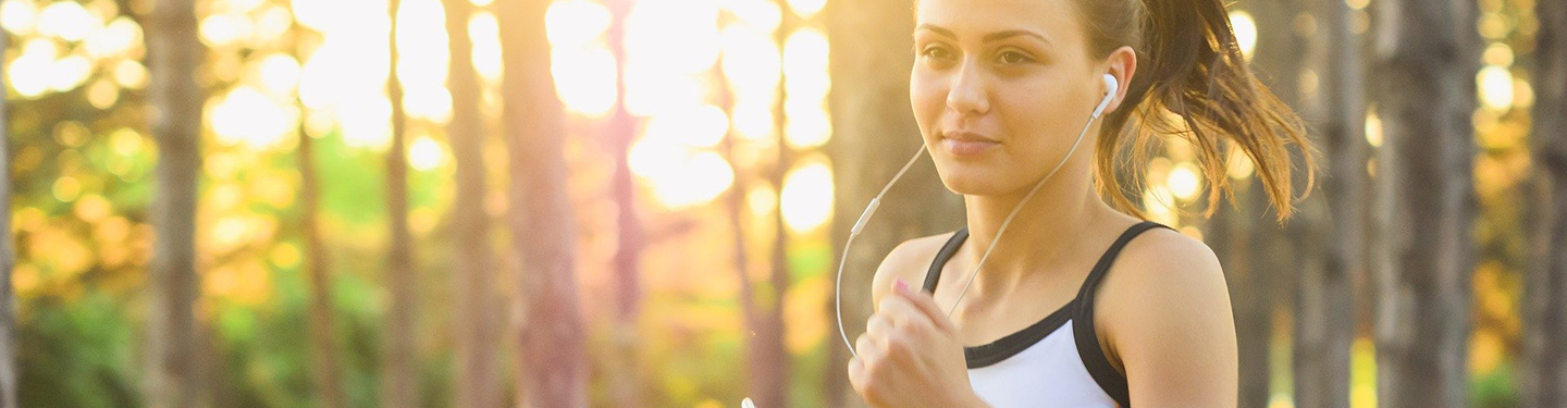 Mujer corriendo con cascos y el atardecer de fondo