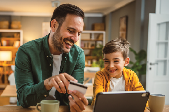 Padre e hijo sonriendo con una tarjeta de crédito y portátil